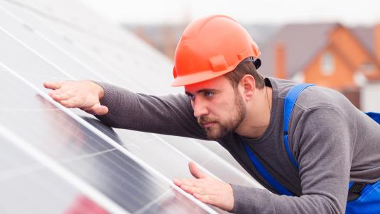 Photograph of a man wearing a hard hat installing solar panels.