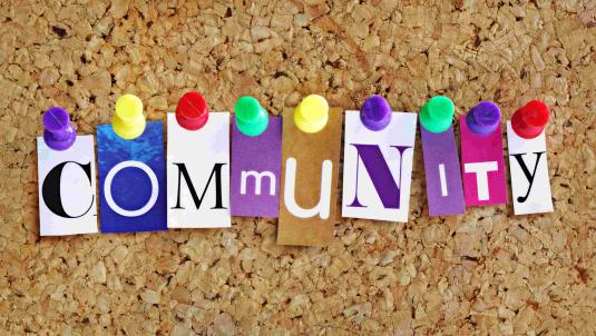 Corkboard with the letters spelling 'Community' in different colours and fonts arranged with coloured pins holding them in place 