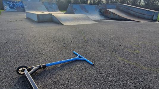 Blue scooter lying on the ground in front of metal skate ramps