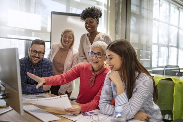 A diverse group of people gathered around a computer in the work place