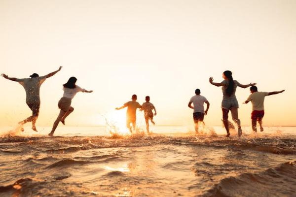 Group of people of different ages running into the sea at sunset