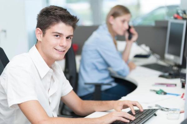 Teenage boy sat at a desk in the work place with colleague