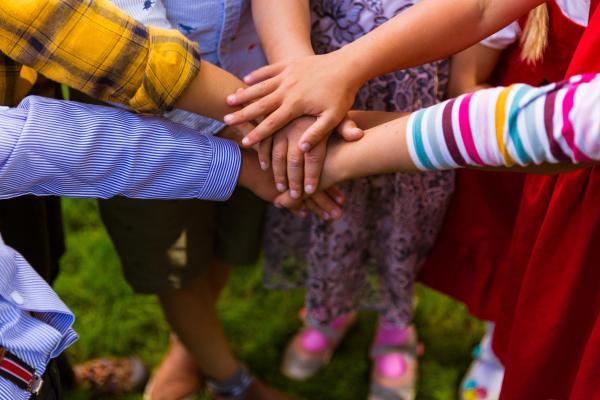 group of children putting their hands on top of each other in a circle