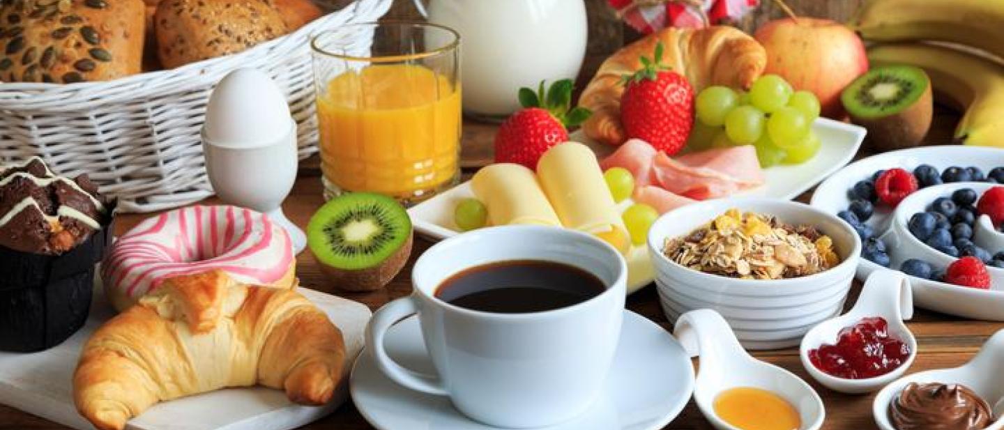 Table with coffee, croissants, fruit, bread and cereal laid out on it.