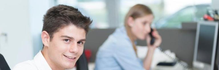 Teenage boy sat at a desk in the work place with colleague