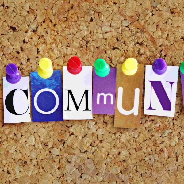 Corkboard with the letters spelling 'Community' in different colours and fonts arranged with coloured pins holding them in place 