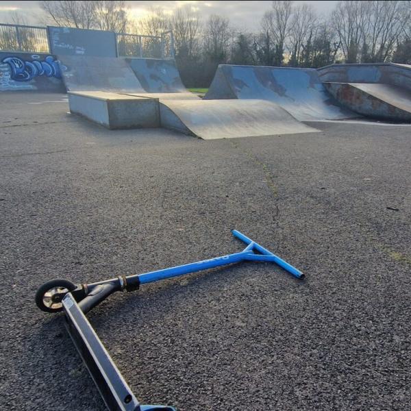 Blue scooter lying on the ground in front of metal skate ramps