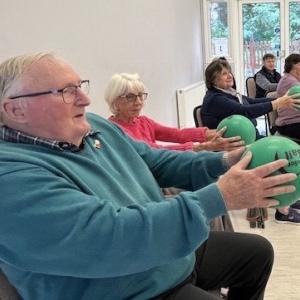 group of older people holding a balance call in front of them doing strength exercises on a chair